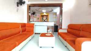 A room with two orange sofas, a white coffee table, and a kitchen area with a refrigerator and a sink. - Dhanas Residency Pondicherry (Puducherry)