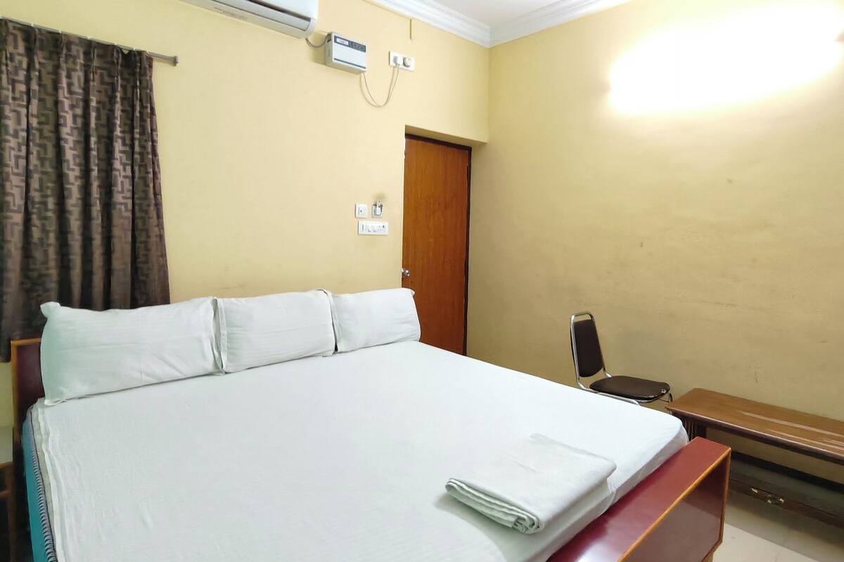 Quarto com cama, um banco, ar condicionado e uma porta.