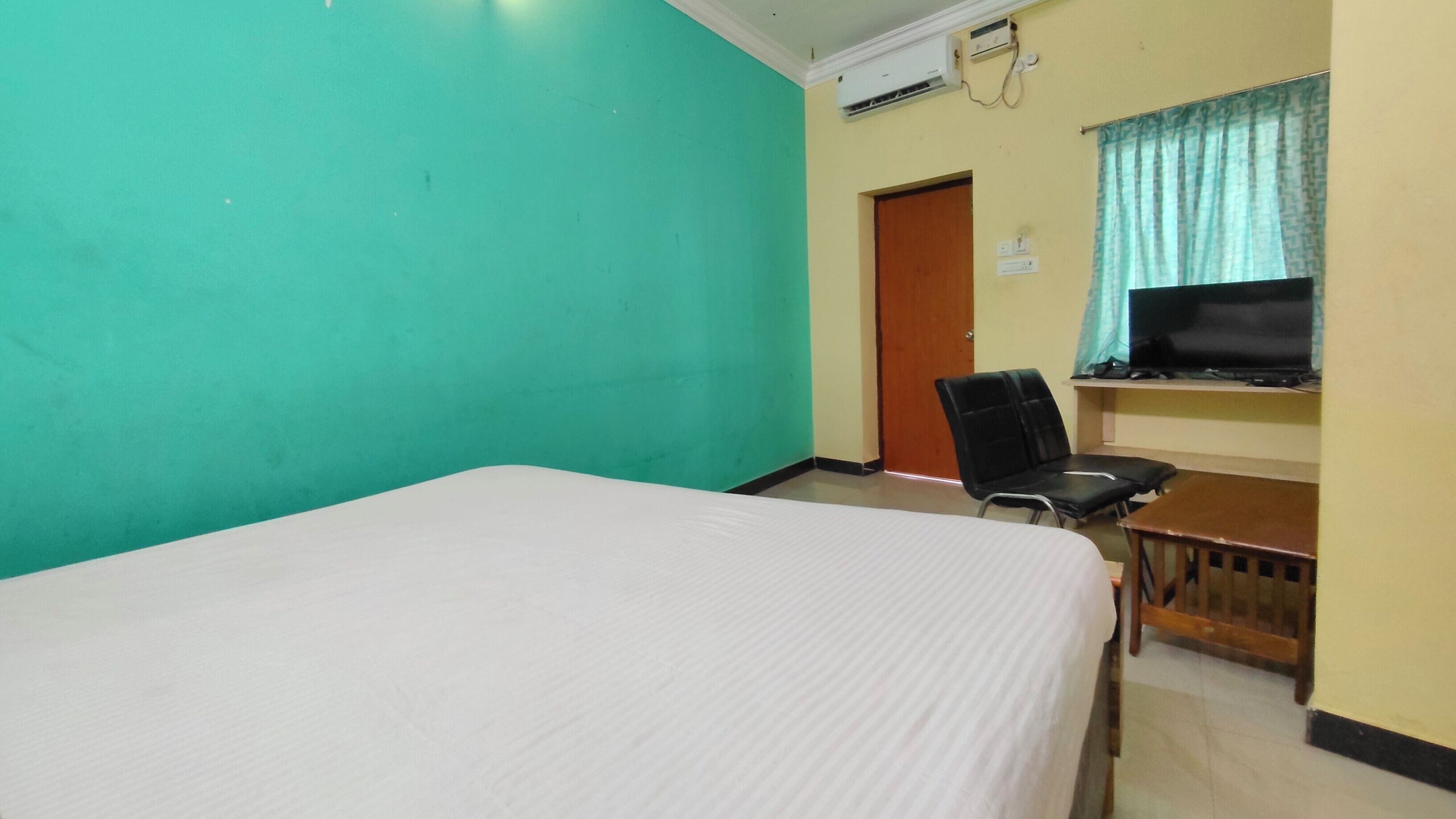 Um quarto com uma cama, uma escrivaninha, uma cadeira, uma televisão e uma porta.