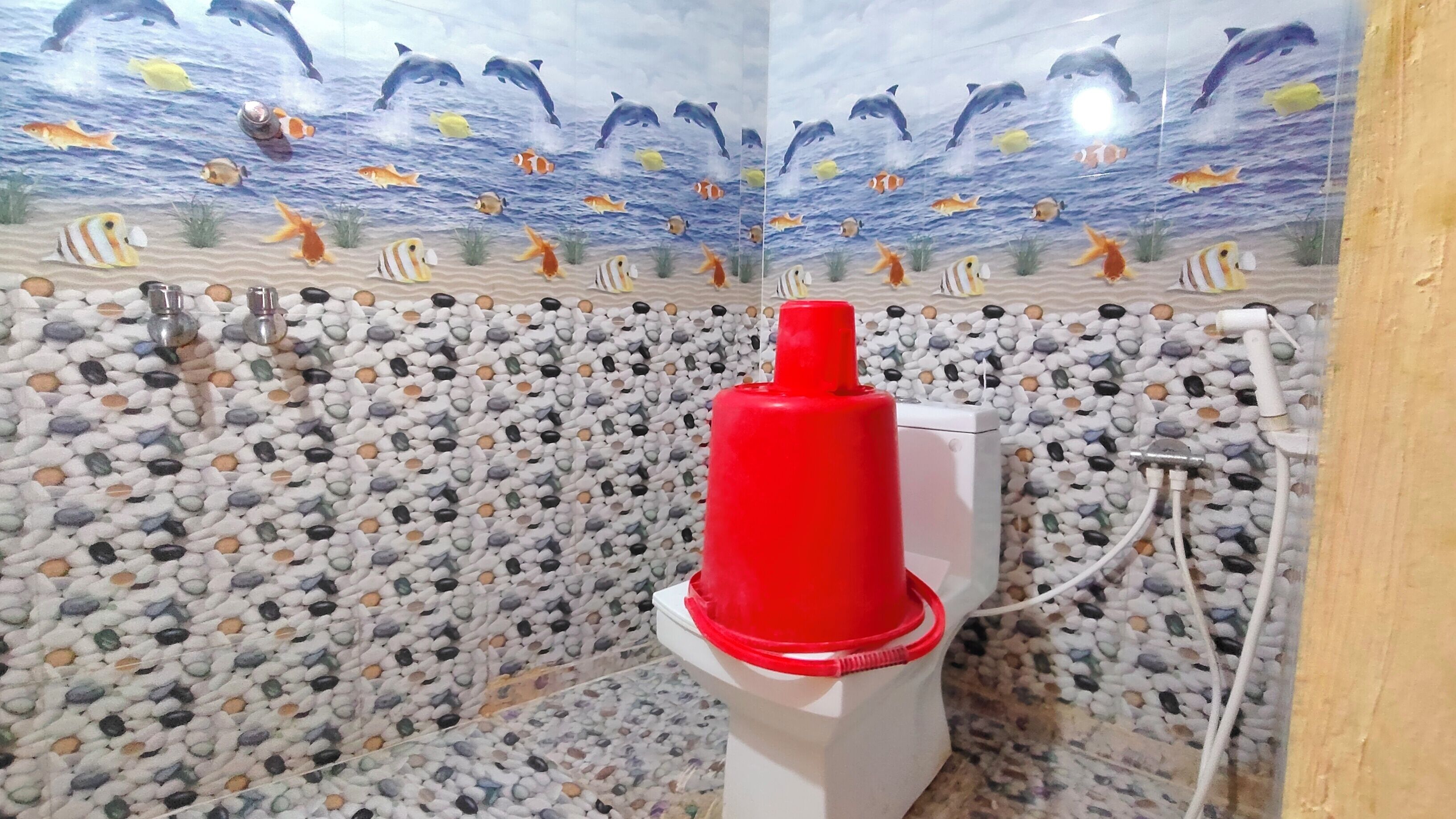 A bathroom with a pebbled floor, a red object on a pedestal, and a wall mural of marine life.