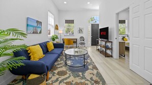 A living room with a blue sofa, a glass coffee table, and a TV on a stand. - Pineapple Paradise #1 • 13 min to Beach • Fire Pit (Sarasota)