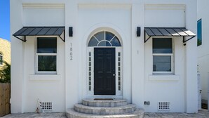 A white building with a black door, numbered 1862, and two windows with awnings. - Pineapple Paradise #1 • 13 min to Beach • Fire Pit (Sarasota)
