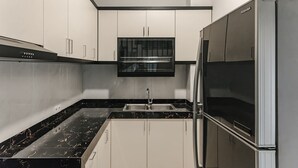 A modern kitchen with white cabinets, a black marble countertop, a stainless steel sink, and a built-in refrigerator. - INNCA Simpang Lima, Semarang (Semarang)