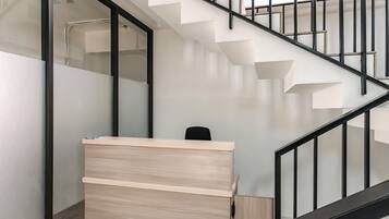 A modern reception desk with a light wood finish, a black chair, and a staircase with black railings.
