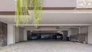 A covered parking area with two cars parked, a hanging plant, and a stone wall. - INNCA Simpang Lima, Semarang (Semarang)