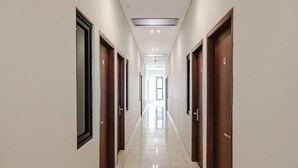 A long, narrow hallway with doors on both sides, leading to a bright room at the end. - INNCA Simpang Lima, Semarang (Semarang)