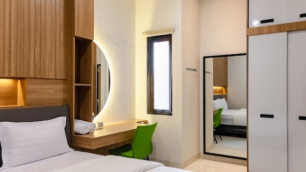 A hotel room with a bed, a desk with a mirror, a green chair, and a wardrobe. - INNCA Simpang Lima, Semarang (Semarang)