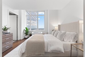 Un dormitorio con una cama grande, un aparador, una ventana con vistas a edificios y una planta en maceta.