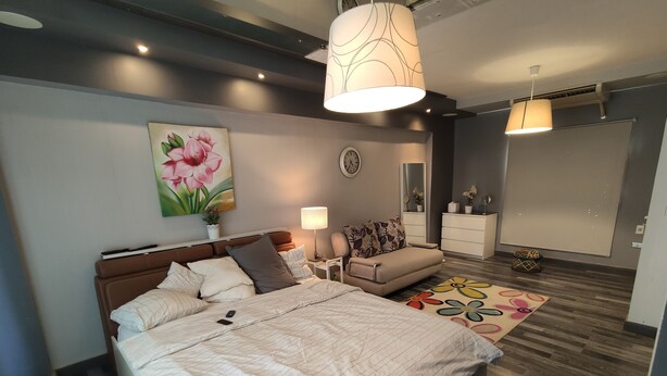 A modern bedroom with a large bed, bedside tables, a sofa, a dresser, and a large mirror. - Villa 56 re (October Gardens)