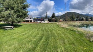 Vista de un lago con una mesa de picnic, un edificio pequeño y montañas al fondo.