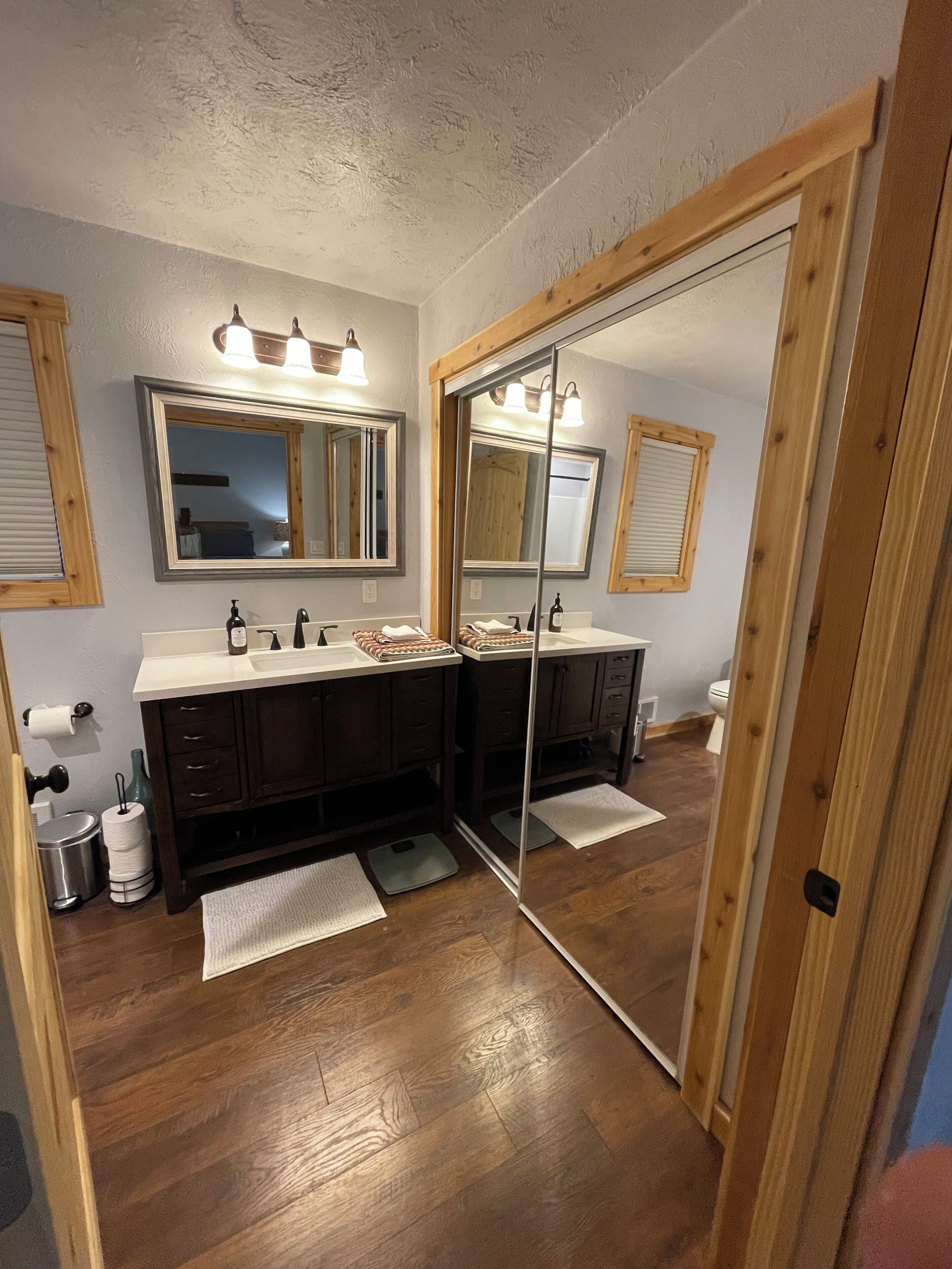Une salle de bain avec un plancher en bois, deux lavabos, un grand miroir et des armoires en bois.