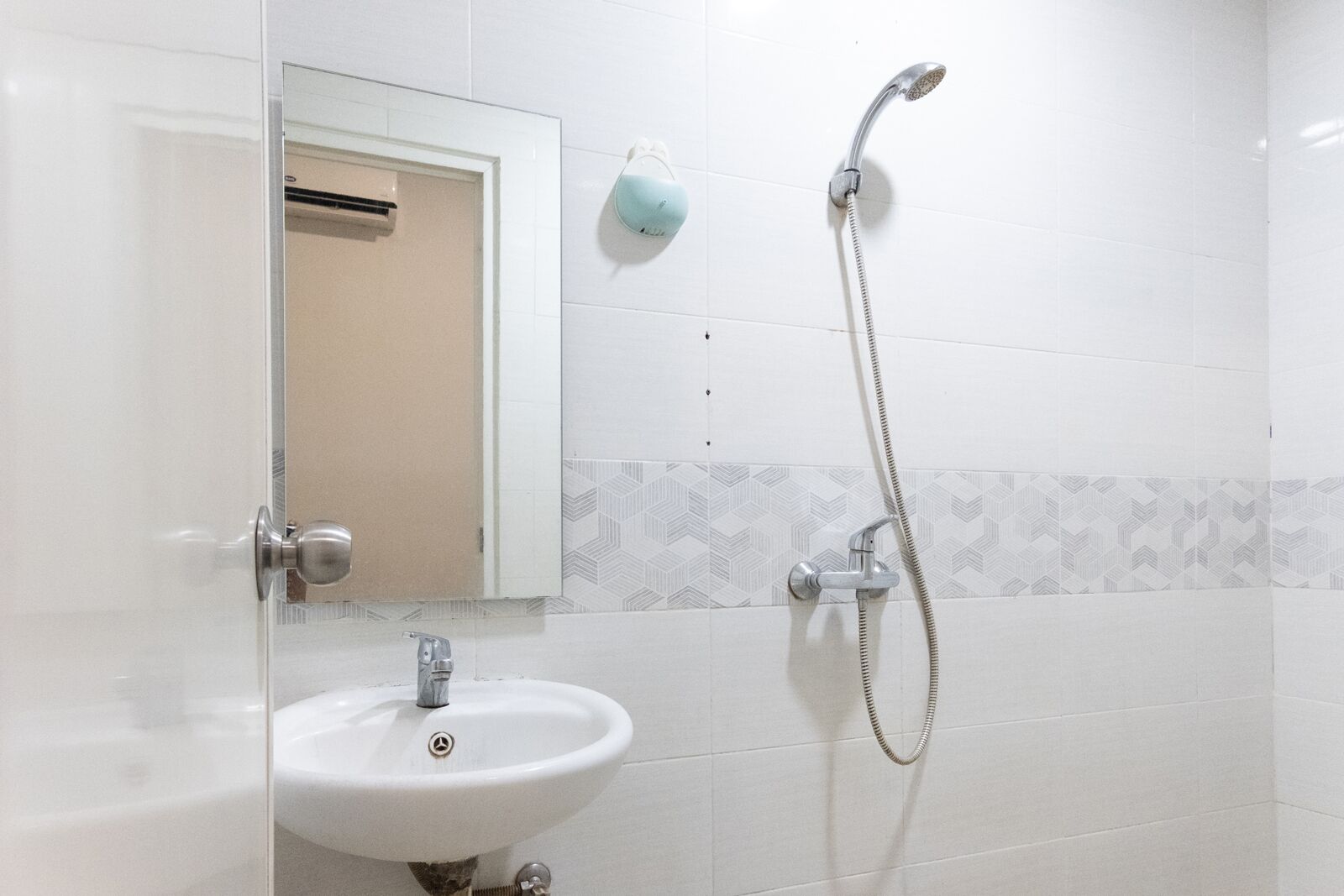 A bathroom with a white sink, a mirror, a shower with a handheld showerhead, and a towel dispenser.