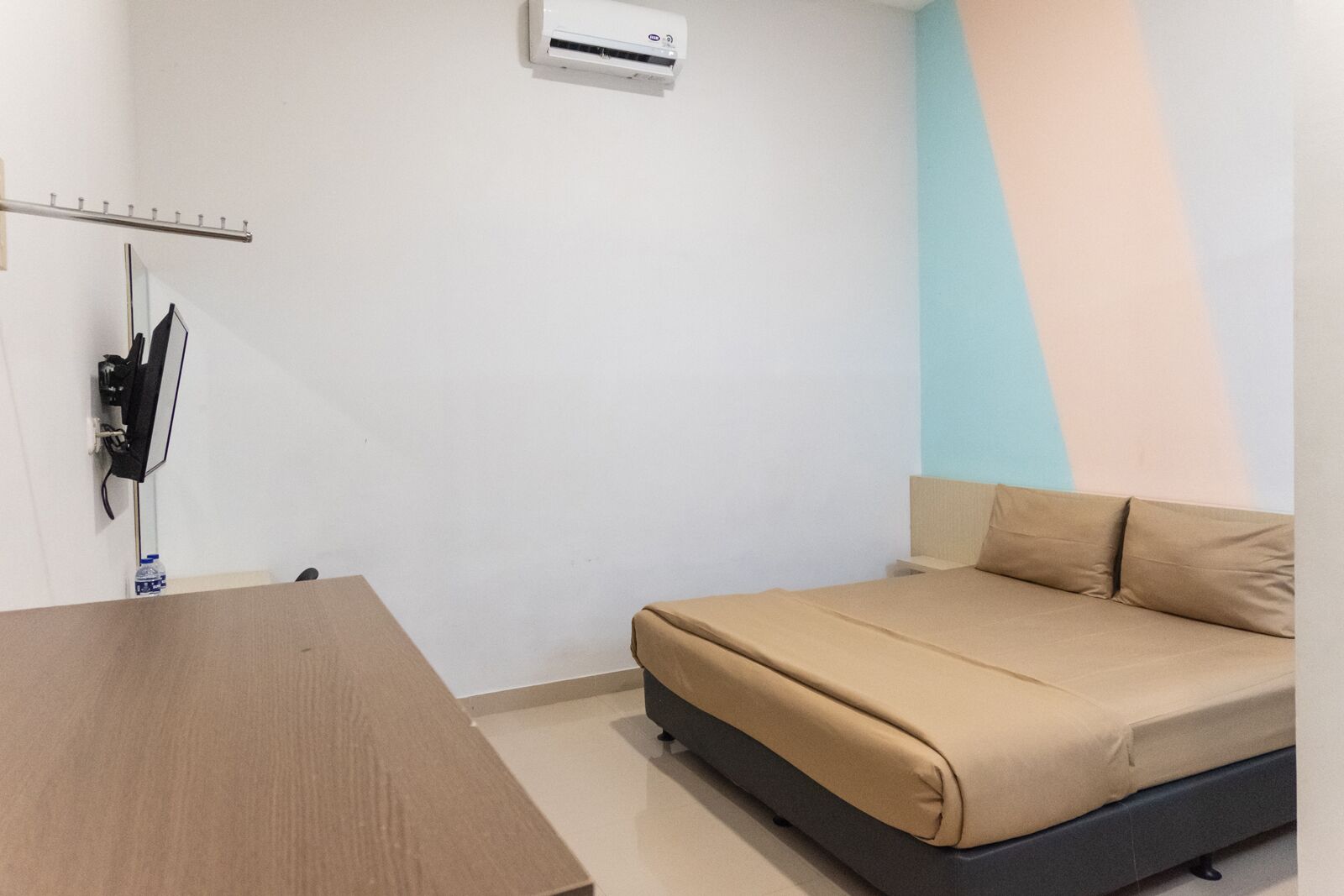 Una habitación pequeña y ordenada con una cama, una mesa y un equipo de aire acondicionado.