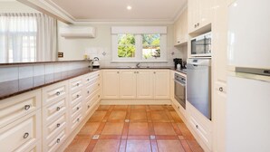 A kitchen with white cabinets, a brown countertop, a window with a view, and a built-in oven. - Porters Cottage Grande (2 units) (Albury)