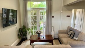 A living room with a large window, a flat-screen TV mounted on the wall, a wooden coffee table, and a beige sofa. - Porters Cottage Grande (2 units) (Albury)