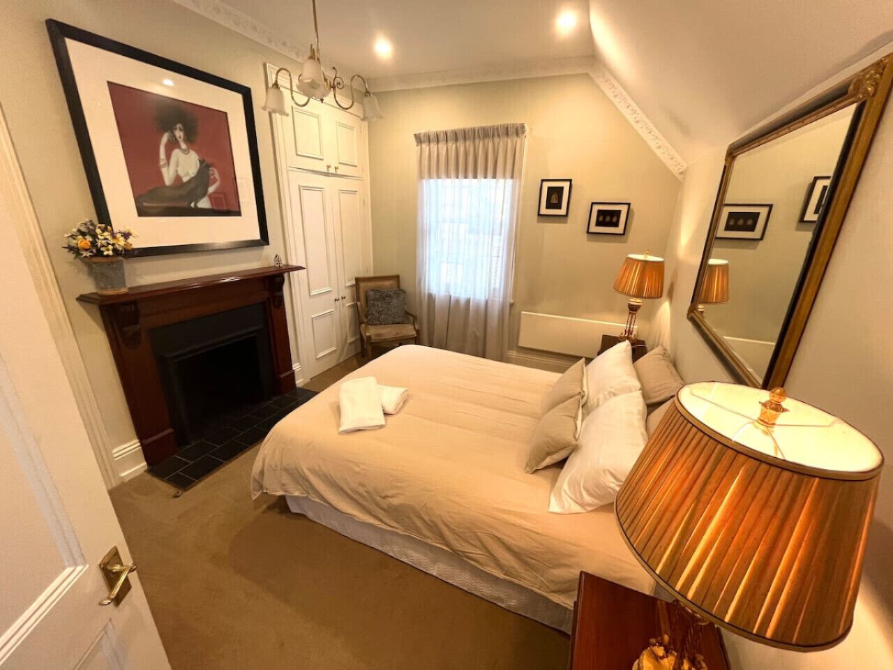 A hotel room with a bed, a fireplace, a mirror, and a lamp. - Porters Cottage Grande (2 units) (Albury)