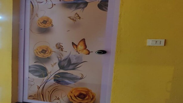 Een deur met een bloemen-en-vlindermotief, een zwarte deurklink en een lichtschakelaar aan de muur.