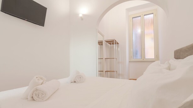 A bedroom with a bed, a TV mounted on the wall, and a window with frosted glass.