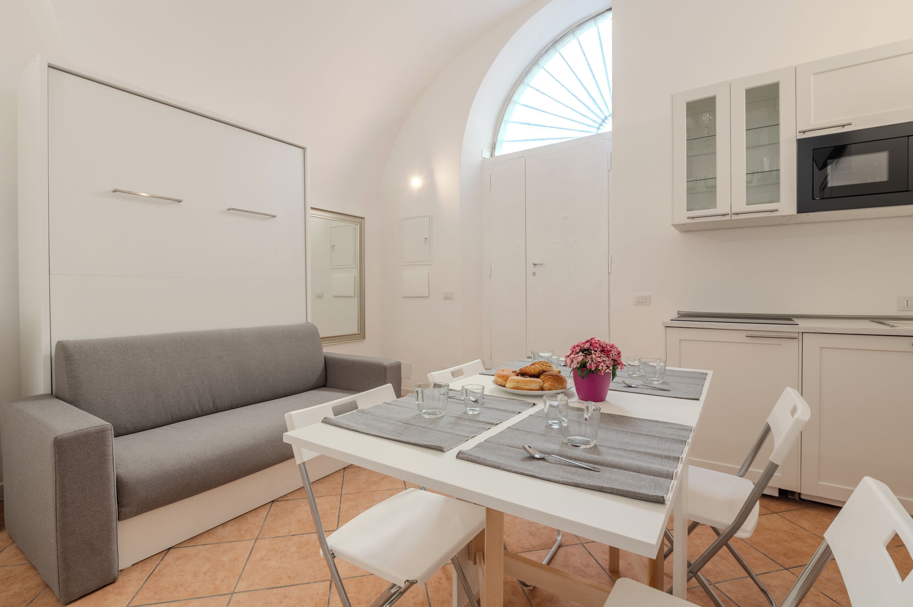 A modern kitchen with white cabinets, a built-in oven, and a dining area with a table set for two.