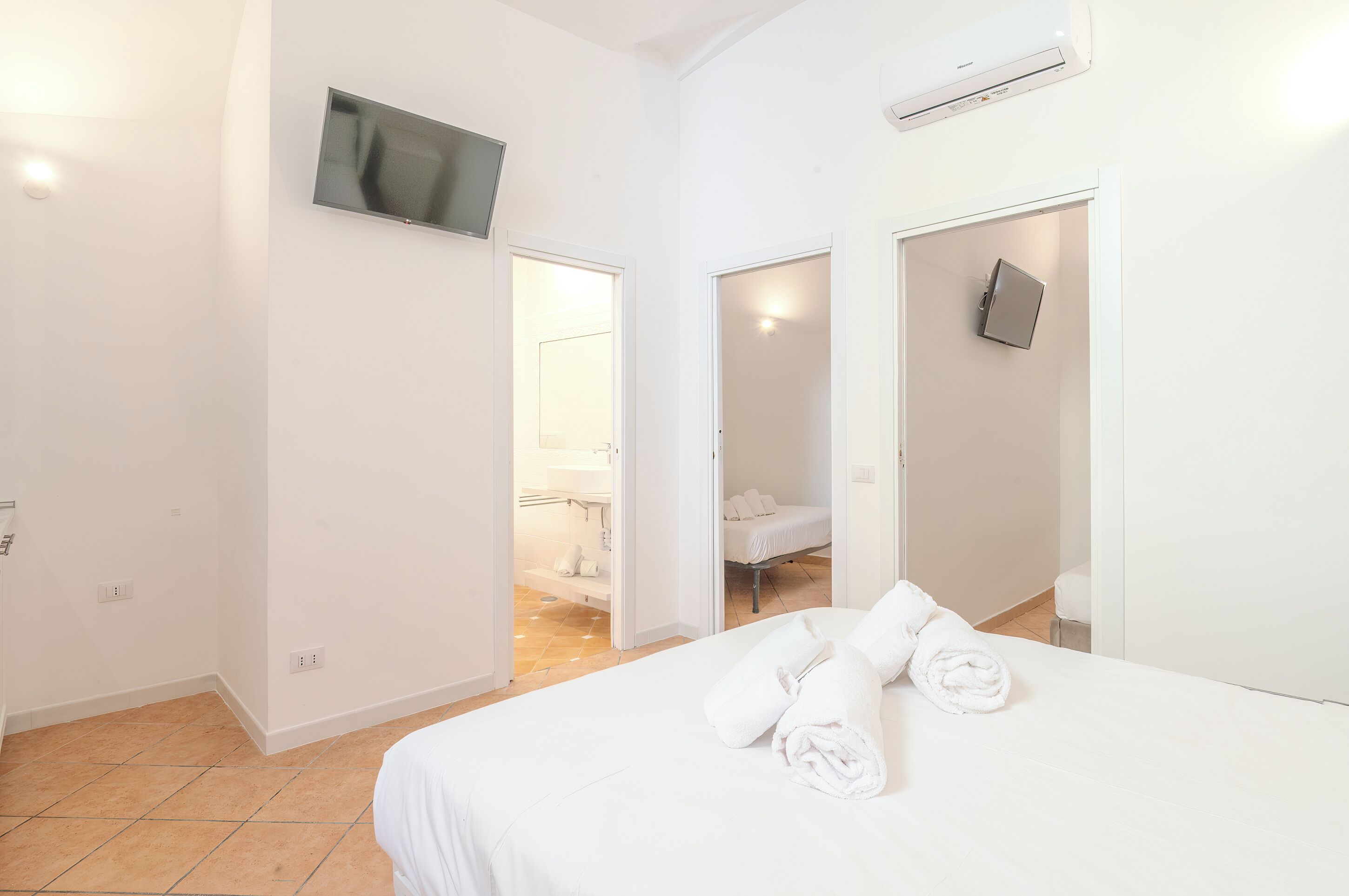 Une chambre d’hôtel avec un lit, un téléviseur fixé au mur et une salle de bain visible à travers une porte ouverte.