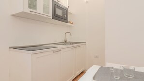 A compact kitchen with a microwave, sink, and a small table with glasses.