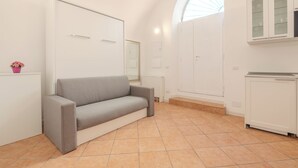 A modern, minimalist room with a grey sofa, white cabinetry, and a large arched window providing natural light.