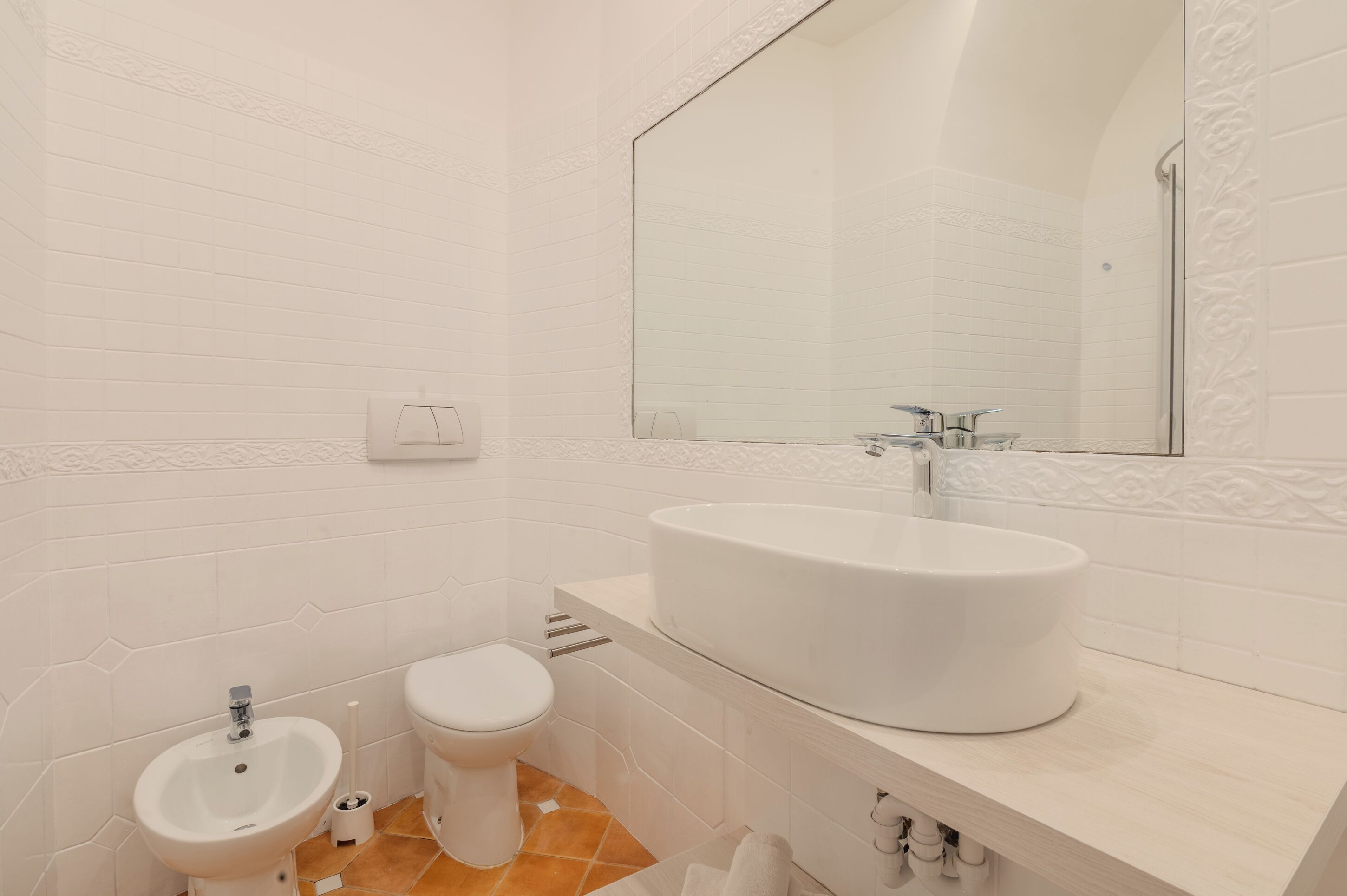A modern bathroom with a large mirror, a white sink, a bidet, and a toilet.