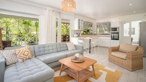 Un salon moderne avec un canapé, une table basse et un fauteuil en osier. Il y a également un coin cuisine avec une table à manger et des chaises.