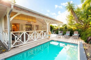 A poolside area with a wooden deck, lounge chairs, and a covered patio.