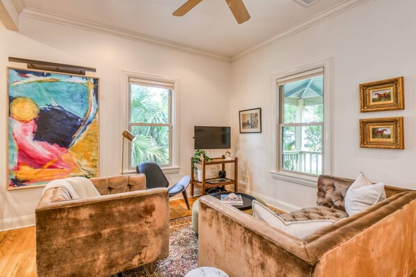 A living room with two sofas, a television, and artwork on the walls. - Charming Cottage, Bike to Downtown Attractions, Private Fenced Yard, Hot Tub, $300 in Free Tickets! (St. Augustine)