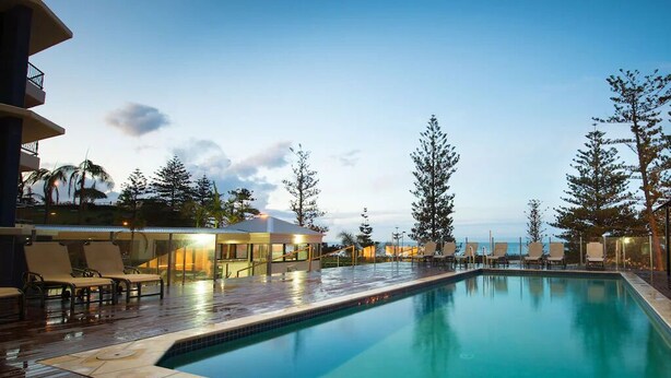 A swimming pool with lounge chairs and a building in the background. - 26Dec 2026 to 2Jan 2027 Beach House Accommodation - New Years (Coolangatta)