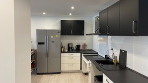 A modern kitchen with black cabinets, a stainless steel refrigerator, a sink, and a countertop with various appliances.