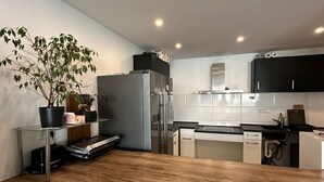A modern kitchen with a wooden island, white chairs, and a potted plant.