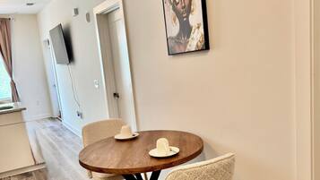 A dining area with a round wooden table, two chairs, and a painting on the wall.