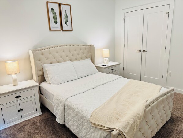 A bedroom with a bed, two bedside tables, a nightstand, a wardrobe, and framed botanical prints on the wall.