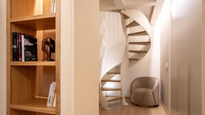 Un interior moderno con una estantería de madera, una escalera en espiral y un sillón gris.