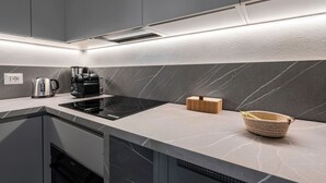 Eine moderne Küche mit einem glänzenden schwarzen Induktionskochfeld, einer Kaffeemaschine und einem gewebten Korb auf der Arbeitsfläche.
