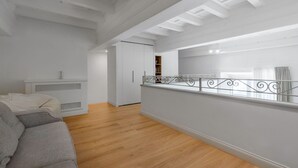 Ein geräumiges Zimmer mit Holzboden, einem grauen Sofa, einem weißen Kleiderschrank und einem Balkon mit Metallgeländer.