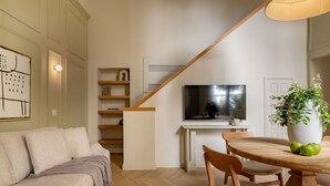 A modern living room with a sofa, a dining table with chairs, a TV, and a staircase.