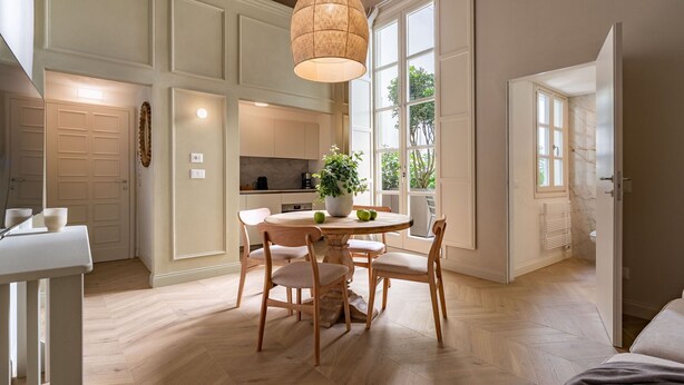 A modern kitchen with a dining area, featuring a round wooden table, chairs, and a hanging light fixture.