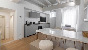 Une cuisine moderne avec des meubles gris, un téléviseur à écran plat et un coin repas comprenant une table blanche et des bancs.