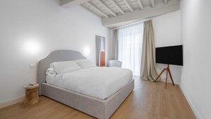 Une chambre moderne avec un grand lit, une table de chevet, un téléviseur posé sur un trépied et une fenêtre avec des rideaux.