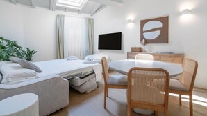 Une chambre d’hôtel moderne, équipée d’un lit, d’une table à manger avec des chaises, d’un téléviseur et d’un grand tableau abstrait accroché au mur.
