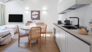 Une cuisine moderne avec des armoires blanches, un évier noir et une cuisinière encastrée. On y trouve également un coin repas avec une table ronde et des chaises en osier.