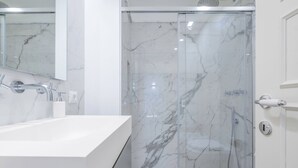 Une salle de bain moderne avec un espace de douche en marbre, un lavabo blanc et une porte de douche en verre.