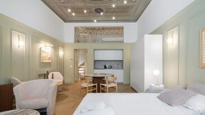 Een hotelkamer met een bed, een zithoek met stoelen, een kleine keuken en een trap.