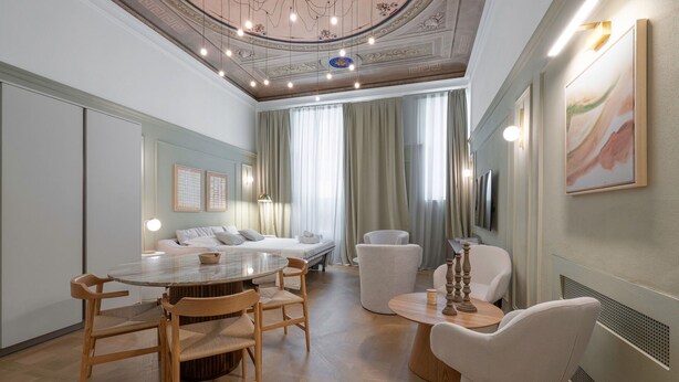 Een ruime kamer met een ronde houten tafel, diverse stoelen, een bank en een bed.