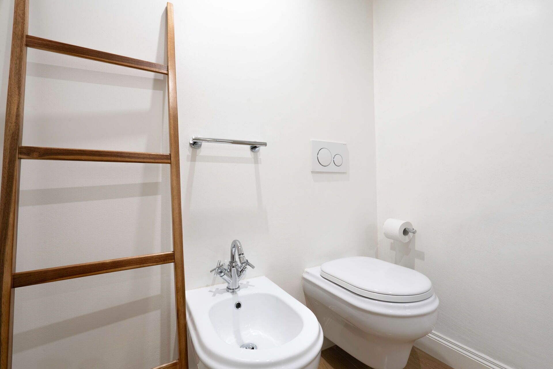 A bathroom with a white sink, a bidet, a toilet, and a wooden-framed mirror.