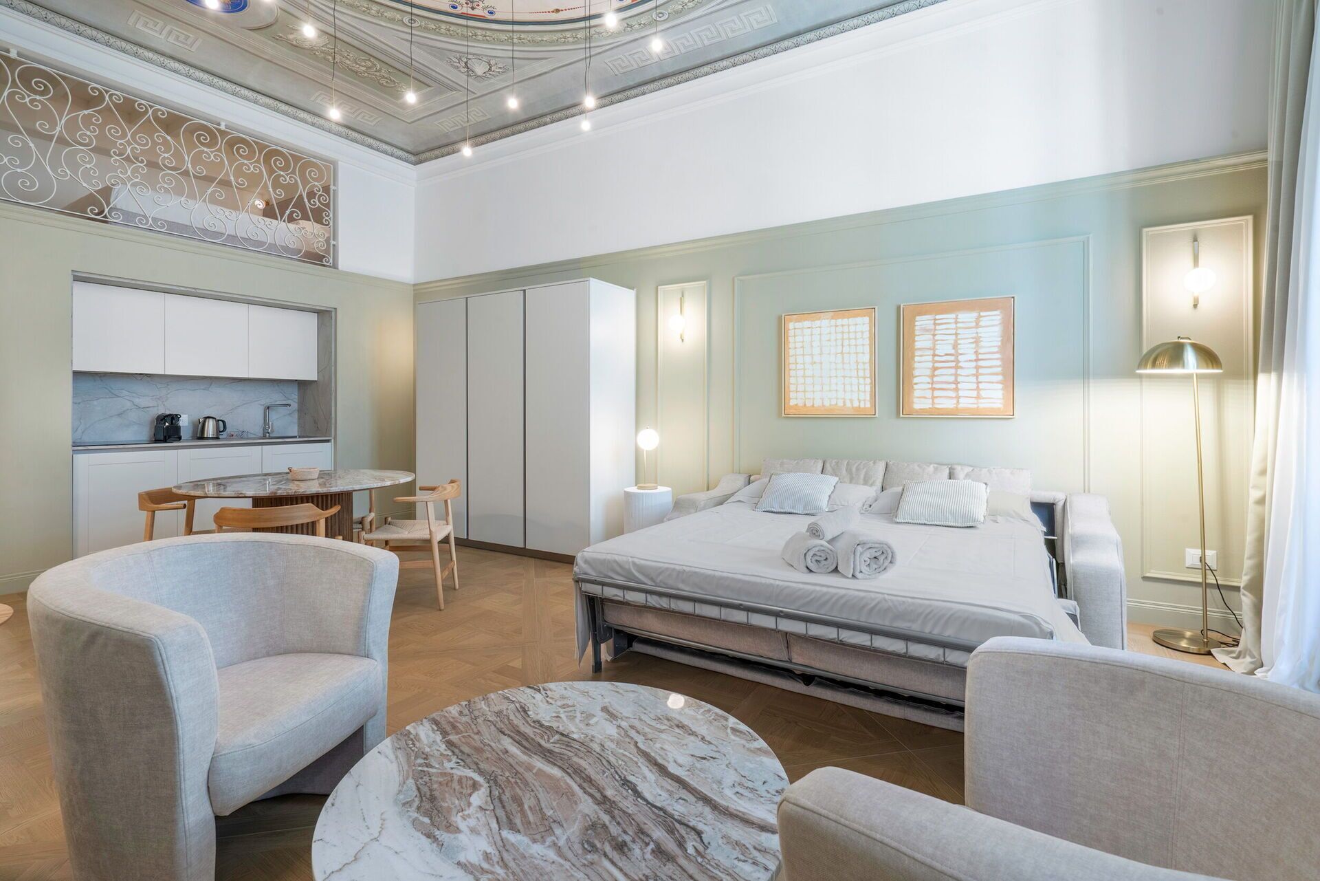 Una habitación de hotel moderna con una cama, dos sillones, una mesa de comedor y una zona de cocina.