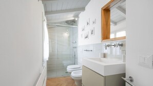 Une salle de bain moderne avec une douche à parois de verre, des toilettes blanches et un meuble-lavabo avec un miroir.